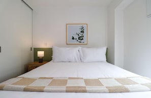 A neatly made bed with a checkered blanket, a bedside lamp, and a framed botanical print on the wall. - w* | Prime 2BR w/ Balcony in Miraflores (Miraflores)