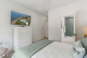 Quarto com cama, penteadeira, televisão exibindo uma paisagem e banheiro com chuveiro.