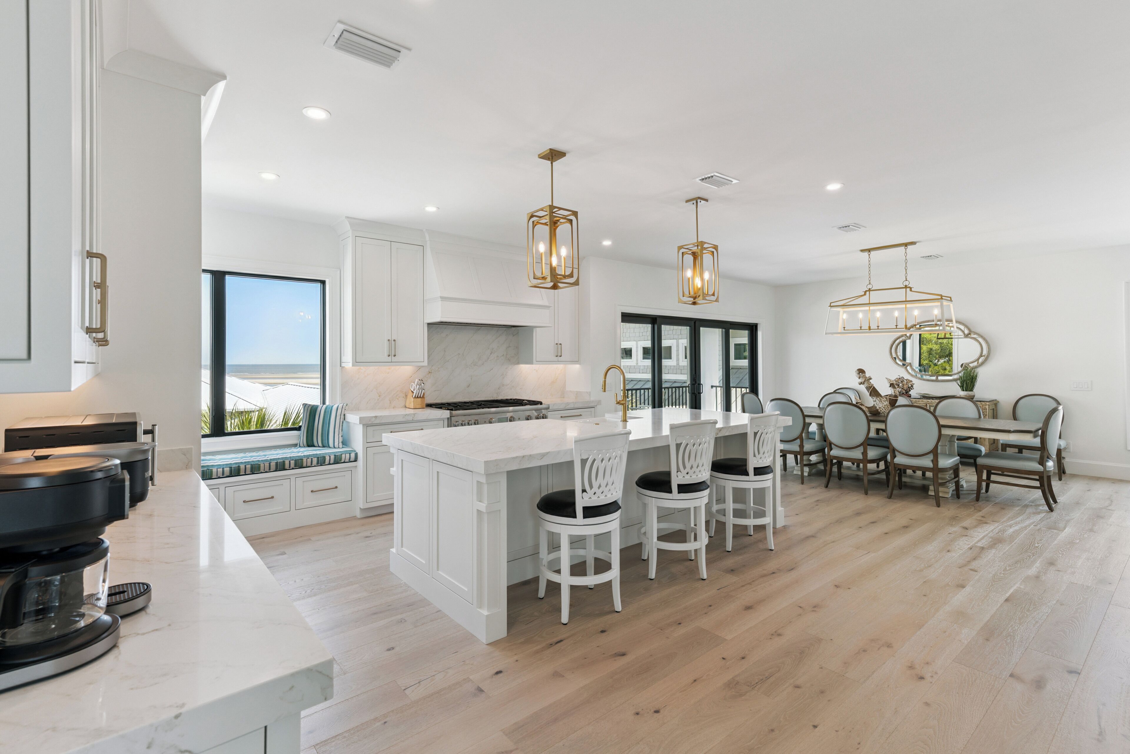 A modern kitchen with a large island, white cabinetry, and a dining area with a view.