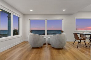 Un comedor con vistas al océano al atardecer, que incluye dos sillones tapizados y una mesa de comedor.