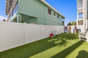 Quintal cercado com grama sintética, um banco branco e um parquinho colorido.