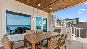 Um deck de madeira com mesa e cadeiras, com vista para uma varanda e o oceano.