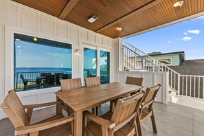 Eine Holzterrasse mit Tisch und Stühlen, die auf einen Balkon mit Meerblick führt.