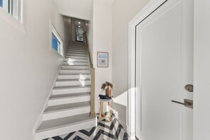 Eine Treppe mit Handlauf, eine Tür mit Schlüsselloch und ein kleiner Tisch mit Vase und Bilderrahmen.