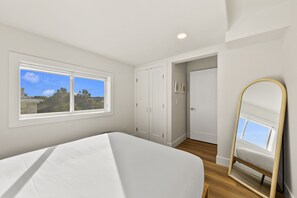 Ein Schlafzimmer mit Bett, Fenster, Kleiderschrank und Spiegel.