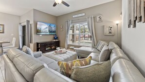 A living room with a ceiling fan, a large window with blinds, a flat-screen TV, and a couch with decorative pillows. - Private Pool *Clubhouse Amenities *BBQ Grill (Kissimmee)