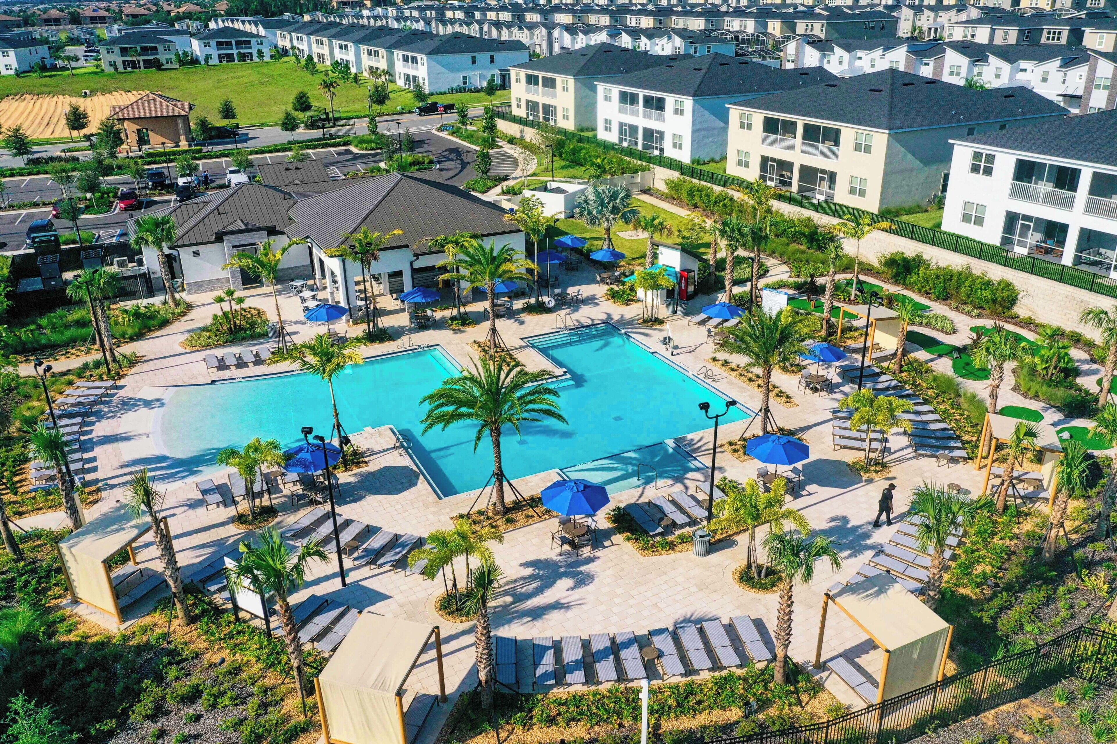 A resort with a central swimming pool, sun loungers, and palm trees.