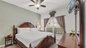 A bedroom with a wooden bed, a nightstand, a bedside table, a ceiling fan, a window with blinds, a mirror, and a wall-mounted TV. - Private Pool *Clubhouse Amenities *BBQ Grill (Kissimmee)