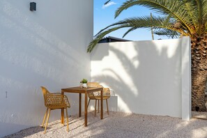 Un espacio al aire libre con una mesa y dos sillas, rodeado por un muro blanco y una palmera.