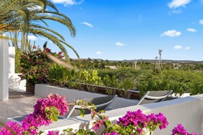 Una terraza en la azotea con sillones blancos, una palmera y flores de buganvilla.