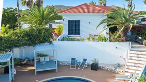 A pool area with lounge chairs and a small building with a red roof. - Grand View: The Room with a Spectacular View (Willemstad)