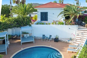 A pool area with lounge chairs and a small building with a red roof. - Grand View: The Room with a Spectacular View (Willemstad)