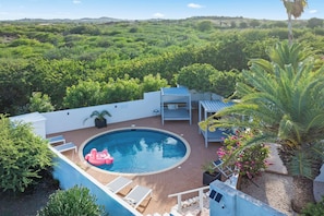 Una piscina circular con un flotador de flamenco rosa, rodeada de sillas de descanso blancas y una pequeña mesa.