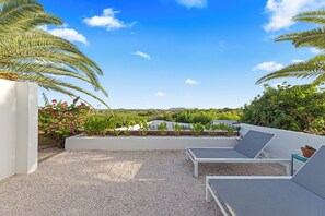 Terraza en la azotea con dos sillones de descanso, suelo de grava y vistas a zonas verdes y edificios a lo lejos.