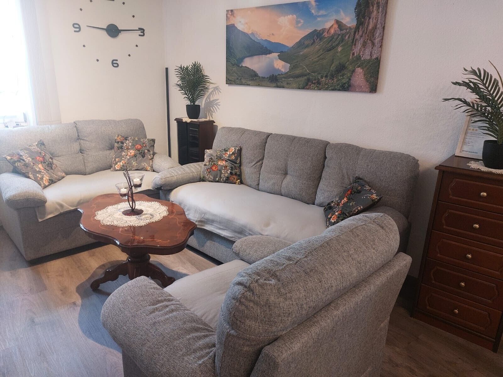 Un salon avec deux canapés gris, une table basse, une horloge, un tableau et un meuble en bois.