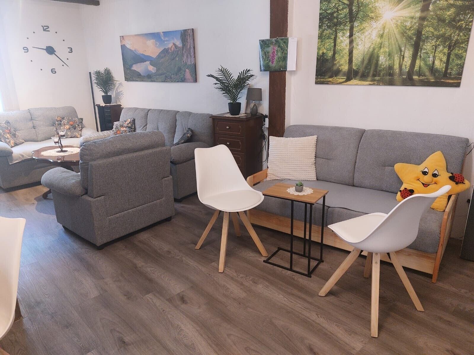 A living room with a grey sofa, two white chairs, a small table, and a star-shaped cushion.