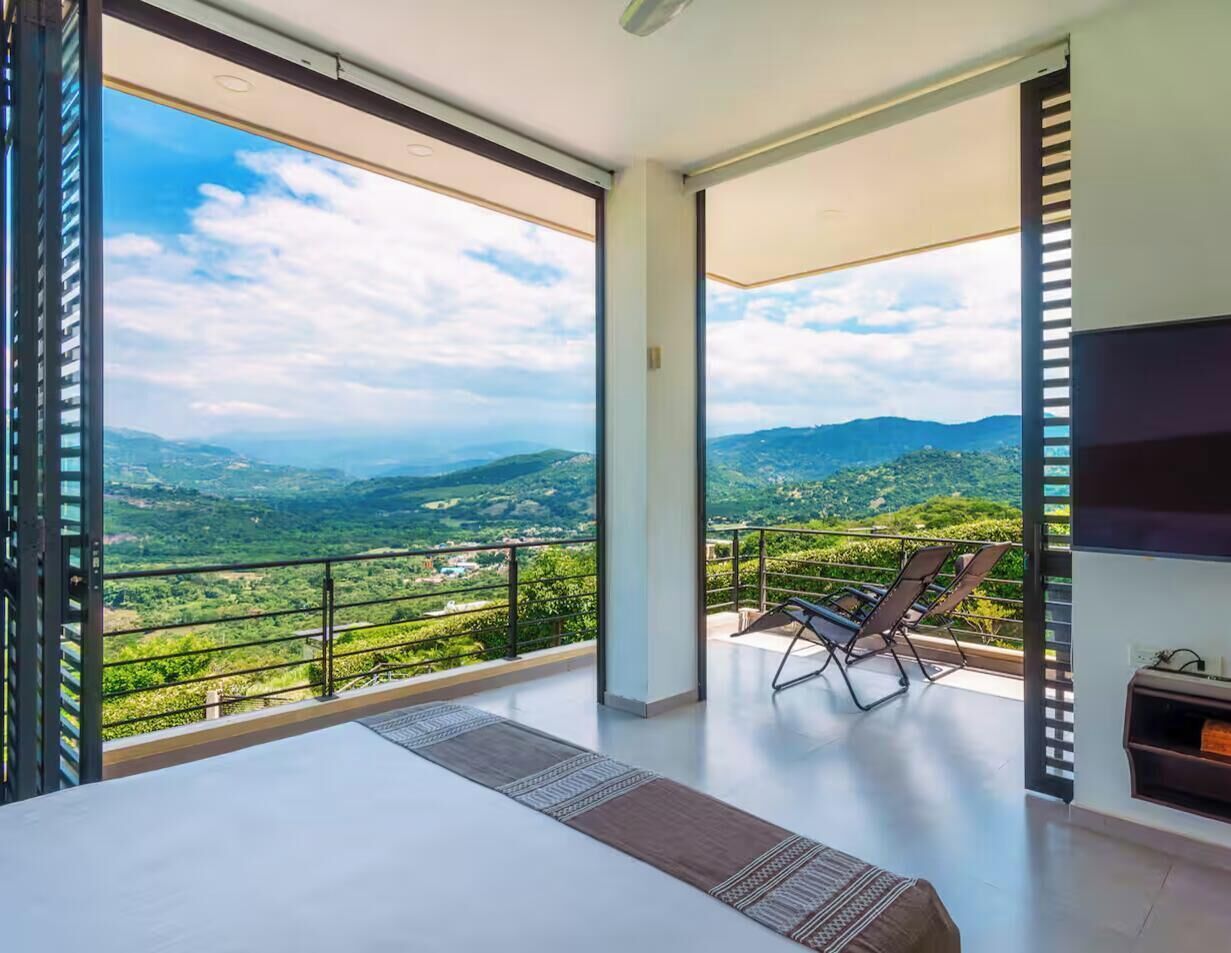 Un dormitorio moderno con una cama grande, televisión y balcón con vistas al campo.