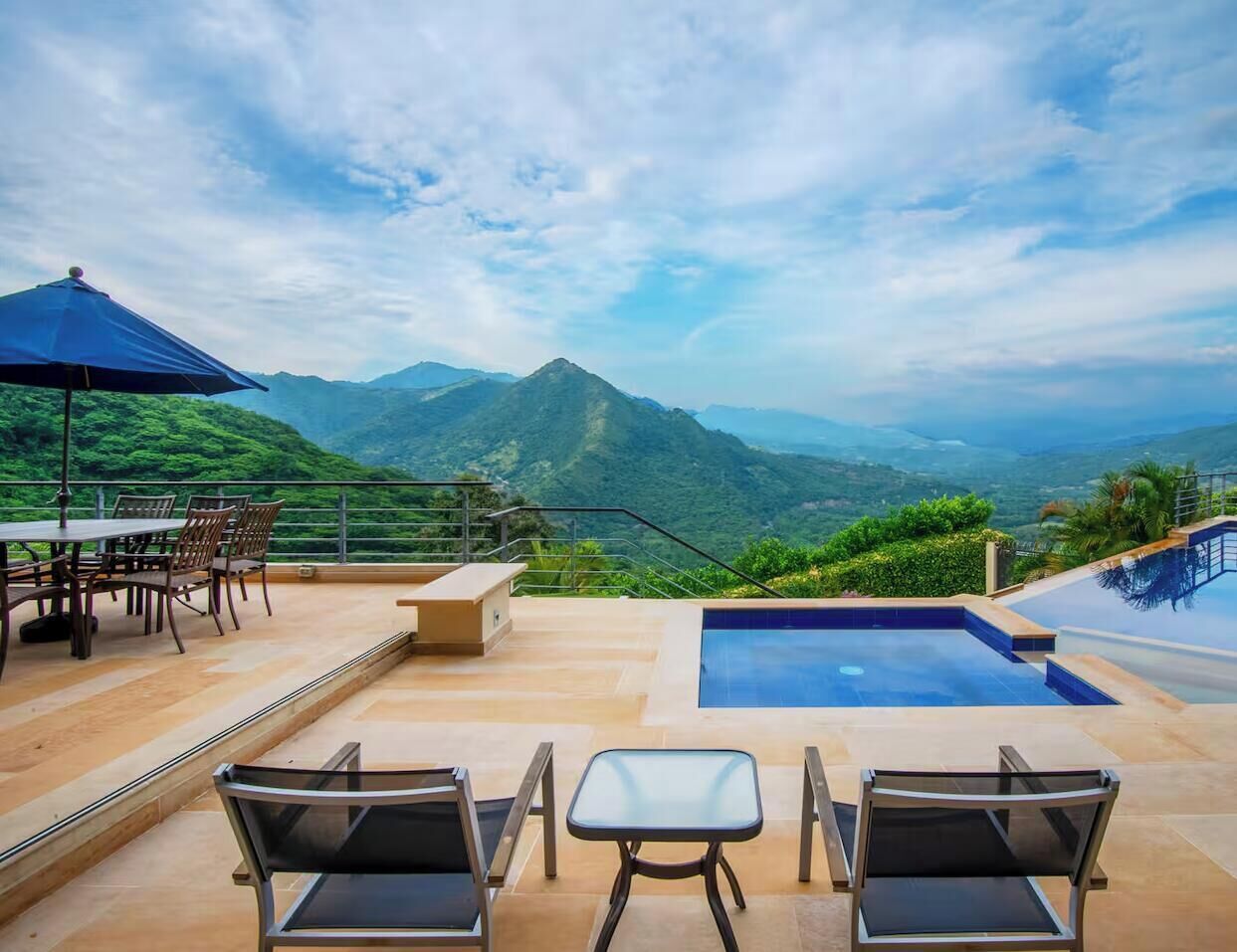 Terraço no telhado com piscina, área de refeições e cadeiras, com vista para uma paisagem montanhosa.