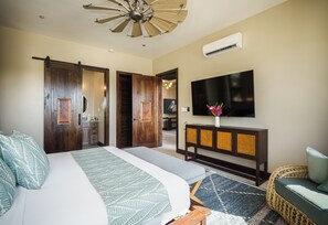 A bedroom with a bed, a TV mounted on the wall, a wooden wardrobe, and a ceiling fan.