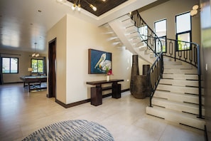 A spacious living area with a wooden floor, a round blue rug, a bench, a painting, and a staircase with a black railing.