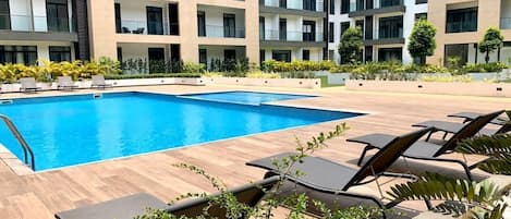 A modern hotel with a swimming pool, lounge chairs, and a courtyard with plants.
