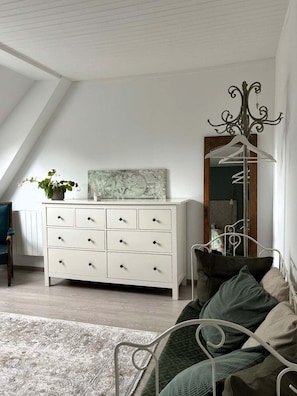 A room with a white dresser, a mirror with a decorative frame, a green sofa, and a patterned rug.