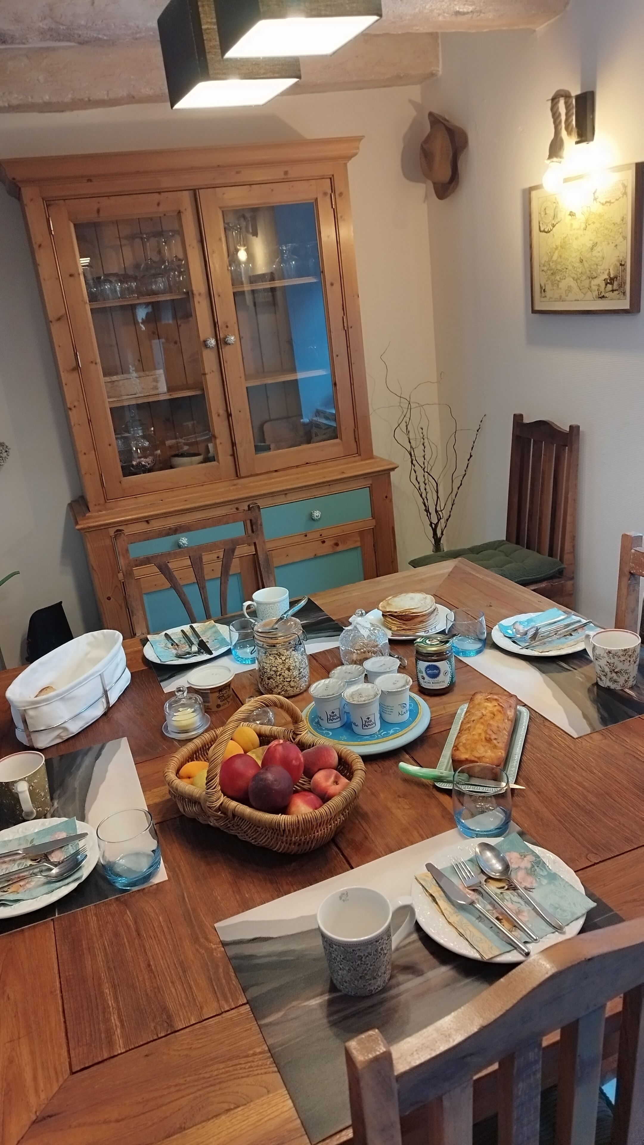 Une table à manger dressée avec des assiettes, des verres et un panier de fruits.