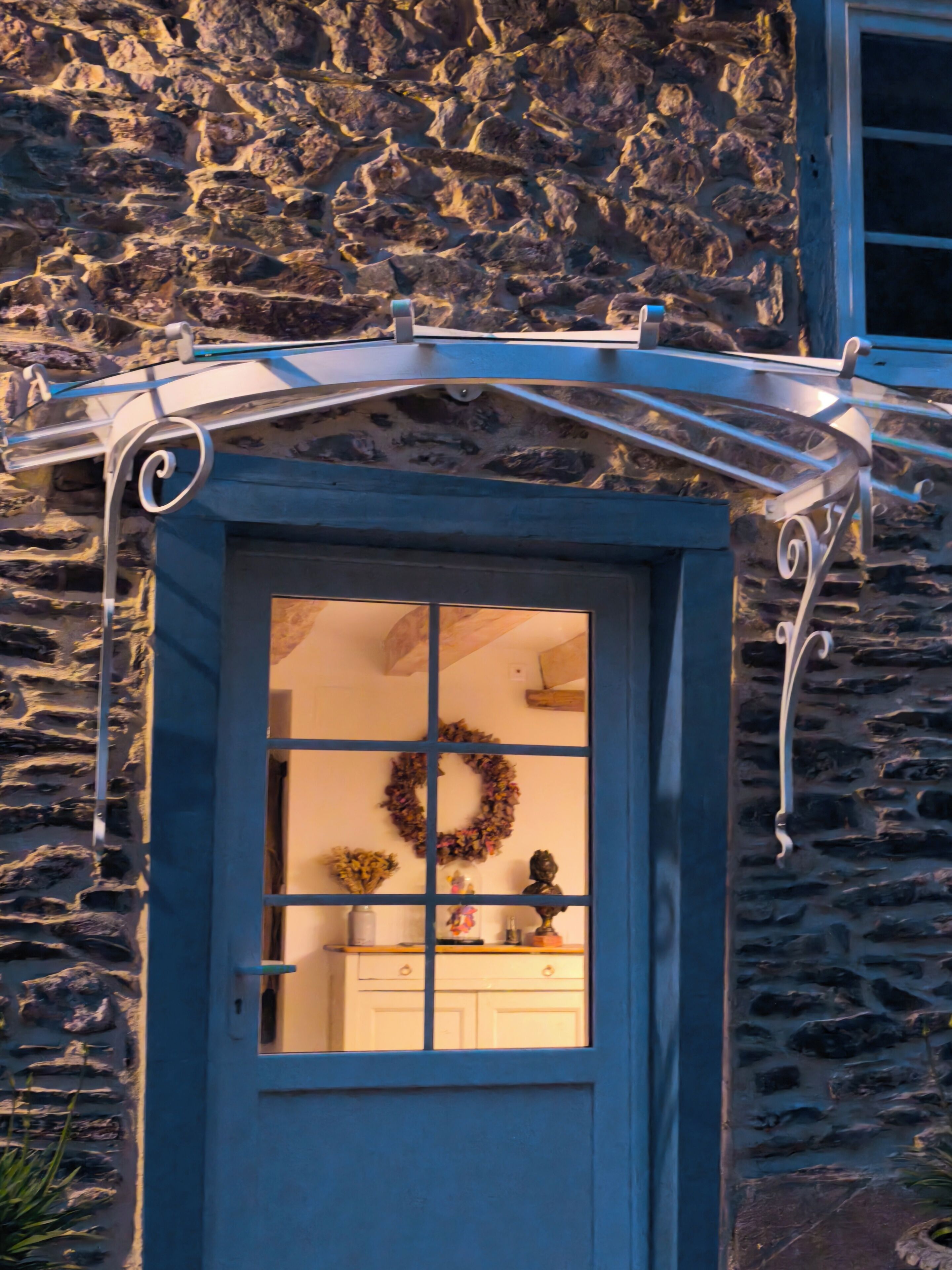Un bâtiment en pierre avec une porte bleue, une guirlande accrochée à la porte et une petite fenêtre au-dessus de la porte.