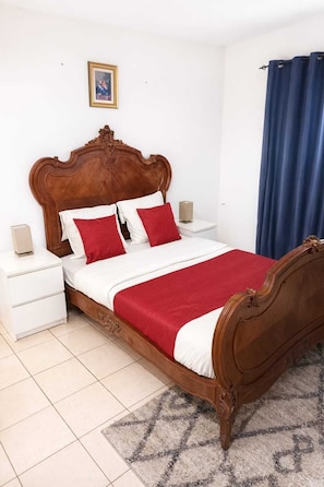 A bedroom with a wooden bed, white nightstands, a red and white bedspread, and a blue curtain.