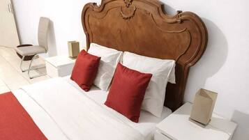 Een hotelkamer met een houten hoofdeinde, een bed met wit en rode beddengoed, een nachtkastje met een lamp en een klein nachtkastje met een doos.