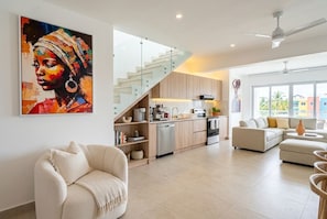 A modern living room with a sofa, a dining area with a kitchen, and a staircase. - Ocean View Penthouse with Private Rooftop (Cabarete)