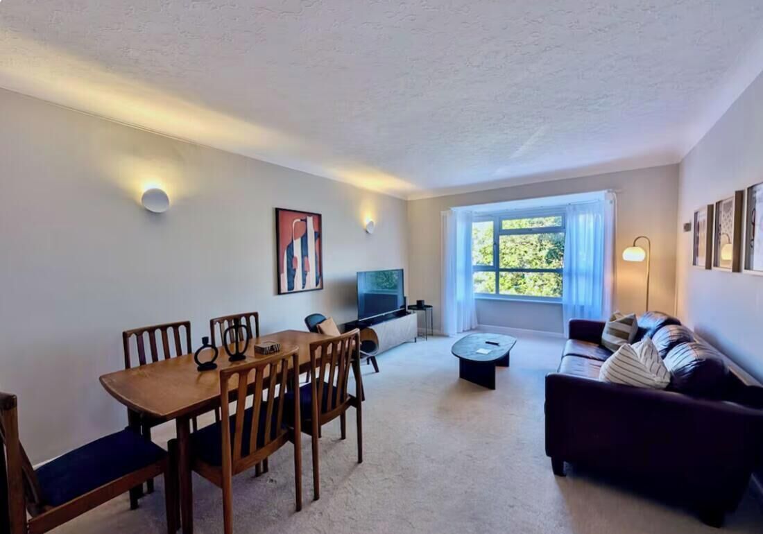 A living room with a dining table, chairs, a sofa, a TV, and a window with curtains.