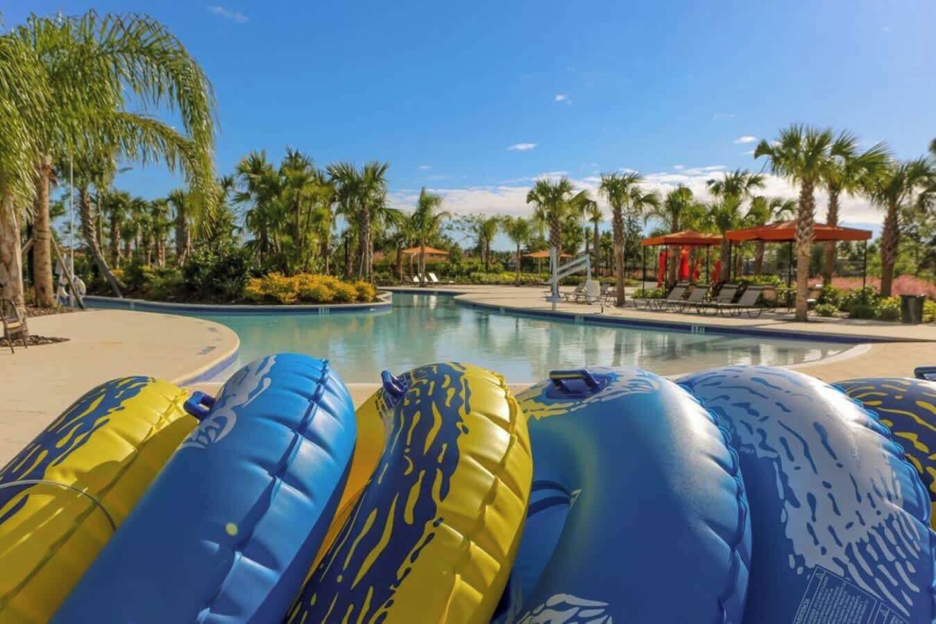 A swimming pool with inflatable rafts, palm trees, and lounge chairs.