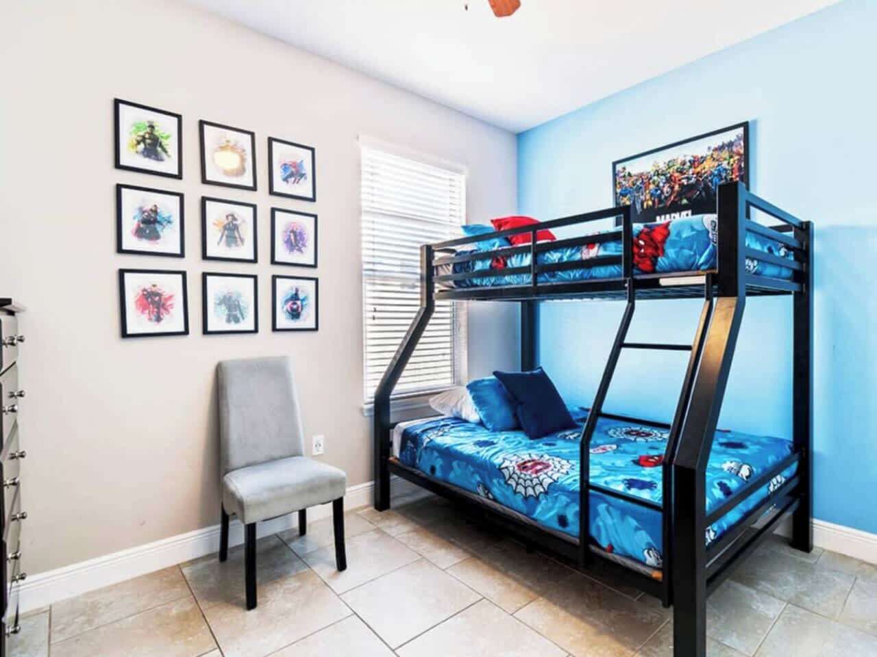 A bunk bed with a blue and red patterned bedspread, a gray chair, and framed artwork on the wall.