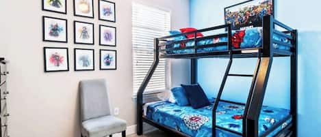 A bunk bed with a blue and red patterned bedspread, a gray chair, and framed artwork on the wall.