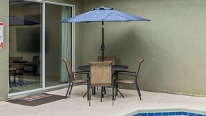 Eine Terrasse mit Tisch, Stühlen und einem blauen Sonnenschirm, sowie ein Schwimmbecken.