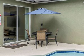 Eine Terrasse mit Tisch, Stühlen und einem blauen Sonnenschirm, sowie ein Schwimmbecken.