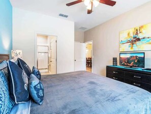 A bedroom with a bed, a ceiling fan, a TV, and a painting on the wall. - Davenport 5BR Pool & Game Room by AllevoHomes (Davenport)