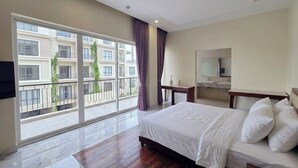 A hotel room with a large bed, a bedside table, a mirror, and a view of a building through a window.