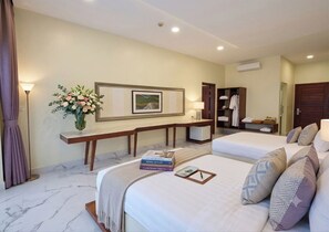 Habitación de hotel con dos camas, un escritorio, una lámpara, un marco de cuadros y un jarrón con flores.