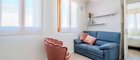 Una sala de estar moderna con un sofá azul, una silla rosa y piso de madera.