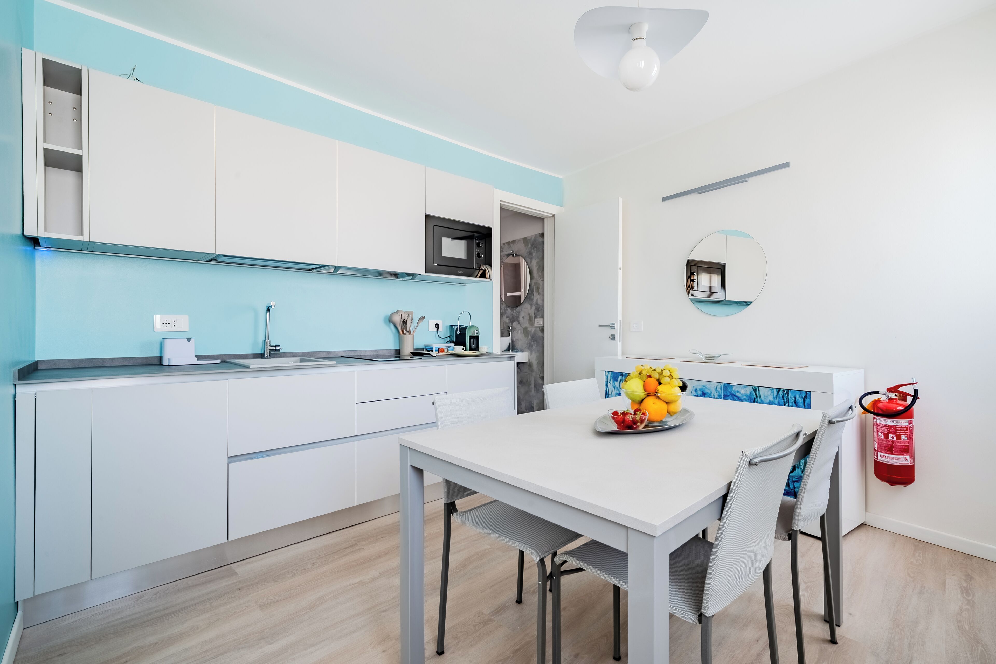 Een moderne keuken met witte kastjes, een ingebouwde magnetron en een eethoek met een tafel en stoelen.