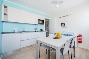 A modern kitchen with white cabinets, a built-in microwave, and a dining area with a table and chairs. - Monet Suite, 100 meters from the Biennale - Canal View (Venezia)