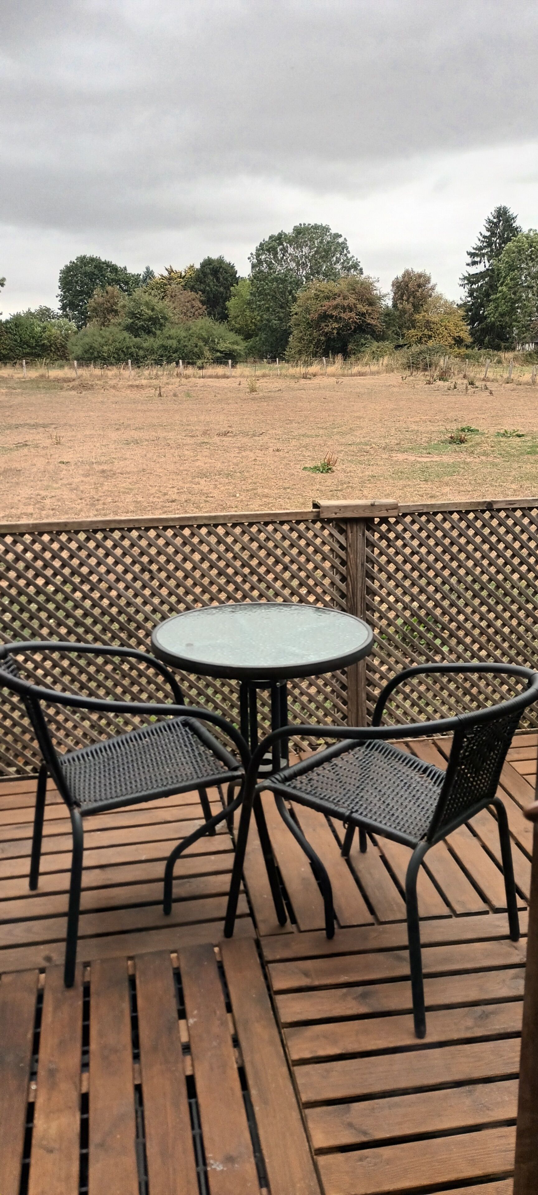 Une terrasse extérieure avec une table ronde et deux chaises, entourée d’une plateforme en bois et d’une clôture à treillis.
