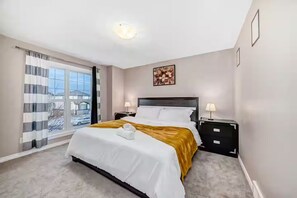 A bedroom with a bed, bedside tables, a window with curtains, and a wall-mounted artwork.