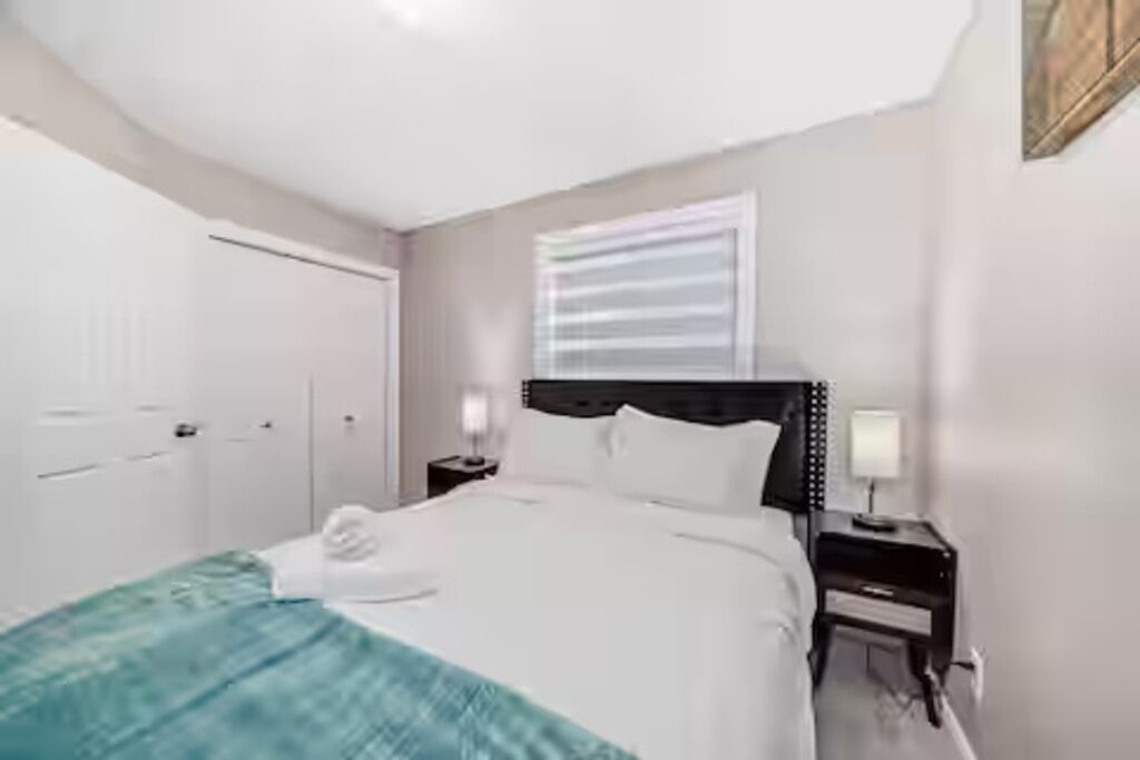Une chambre d’hôtel avec un lit, des tables de chevet, une petite table et une fenêtre avec des stores.