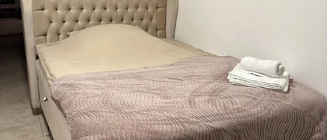 A bed with a tufted headboard, a beige mattress, and a folded white towel on the footboard.