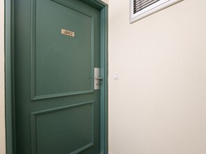 Eine grüne Tür mit Nummernschild, Türgriff und Lichtschalter an der Wand.