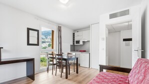 Espai vital compacte amb zona de dinar, petita cuina i llit amb llençols estampats.