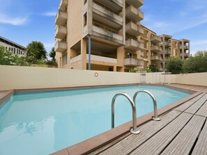A swimming pool with a wooden deck and metal railings, surrounded by a beige building with balconies. - Apartment with balcony and swimming pool (Grasse)